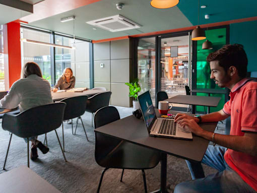 A man in a pink shirt is working on a laptop in a modern office space.