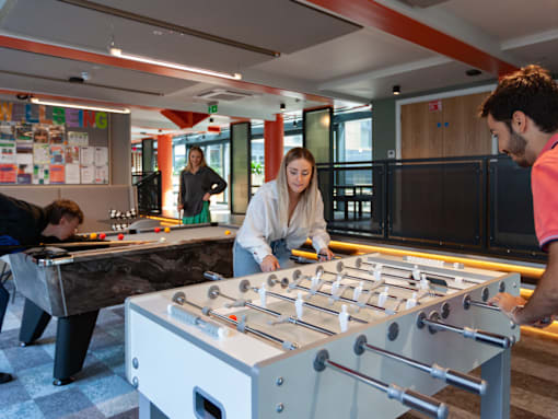 A man and a woman are playing foosball in a room with a ping pong table and other foosball tables in the background.