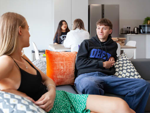 A young man in a black hoodie is sitting on a couch with a woman in a black tank top and a green skirt.