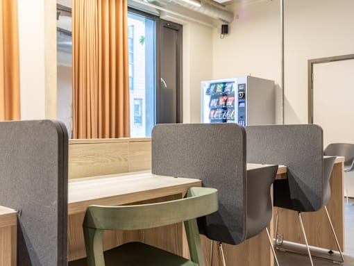 A room with a table and chairs and a fridge in the background.