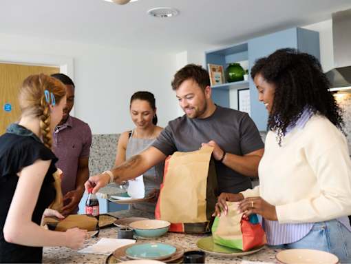 A group of people are gathered around a kitchen counter, preparing food together.