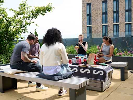 A group of people are sitting around a picnic table on a rooftop.