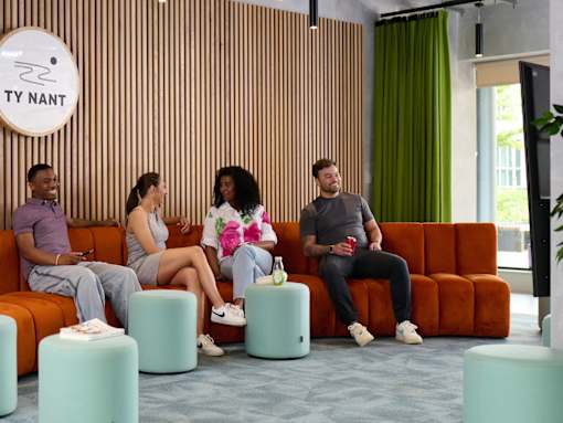 Four people sitting on a couch in a room with a wooden wall and a sign that says "TY NANT".
