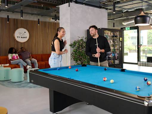 A man and a woman are playing pool in a room with a pool table.