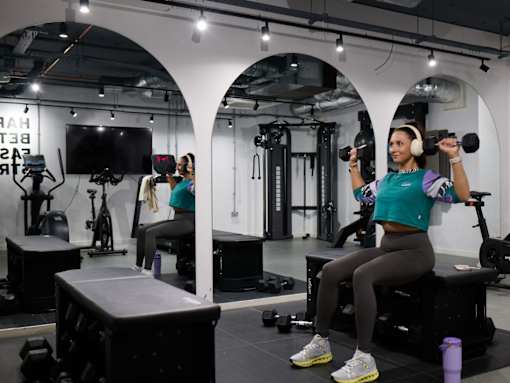 A woman is exercising in a gym with a dumbbell.