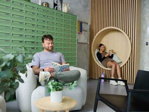 A man is sitting on a white couch reading a book.