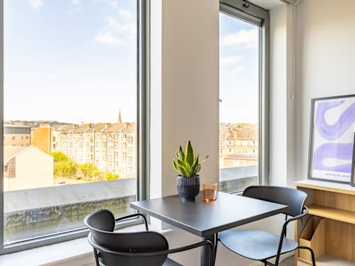 A table with a potted plant and a glass on it sits in front of a window with a view of a cityscape.