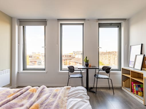 A bedroom with a bed, table and chairs, and a window overlooking a cityscape.