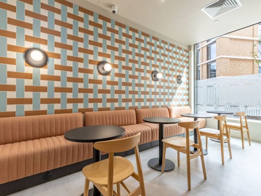 A room with a wall of patterned tiles and a row of chairs and tables.