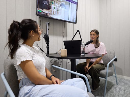 Two women are sitting at a table in front of a television screen.