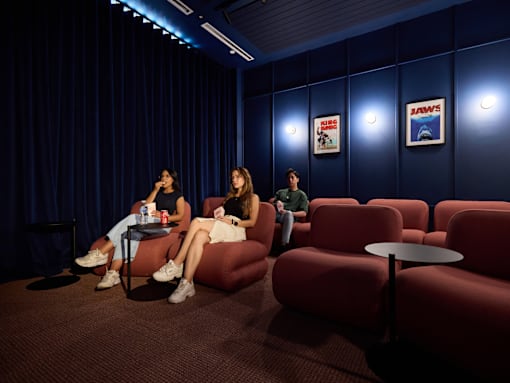 Three people are sitting in a room with red chairs and a blue wall.