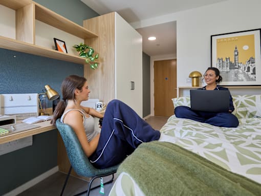 A woman is sitting on a bed with a laptop in front of her.