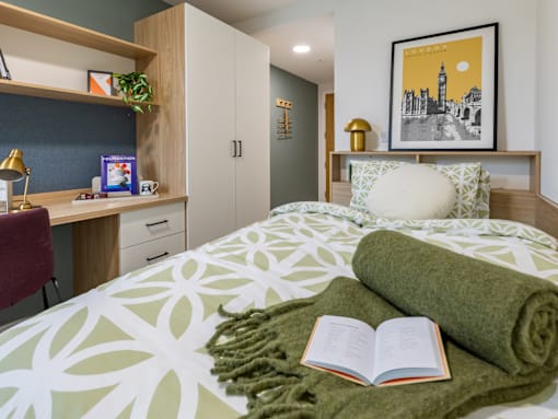 A bedroom with a bed, a desk, and a book on the bed.