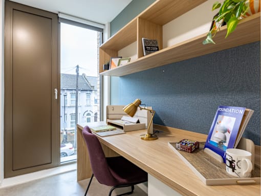 A desk with a chair, lamp, and a book titled "Foundation" is in a room with a window.