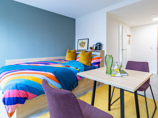 A bedroom with a colorful bedspread and a purple chair.