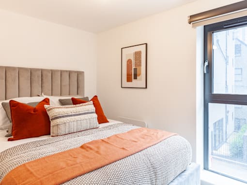 A bedroom with grey and orange bedding.