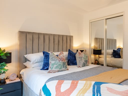 Bed with multi-coloured bedding, headboard and mirrored wardrobe.