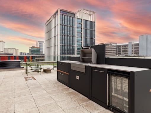 A rooftop patio with a grill and a large building in the background.