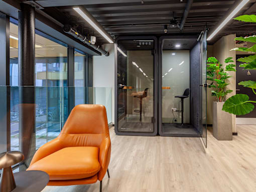 A modern office space with a glass wall and an orange chair.