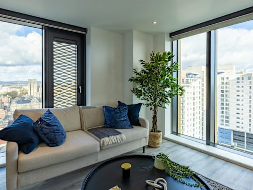A living room with a couch, a potted plant, and a view of the city.