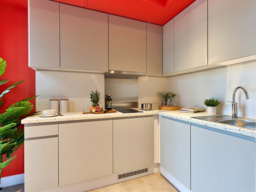 A kitchen with white cabinets and a red wall.