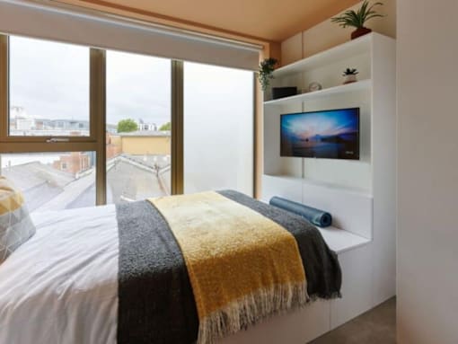 A bedroom with a bed, a television, and a window overlooking a cityscape.