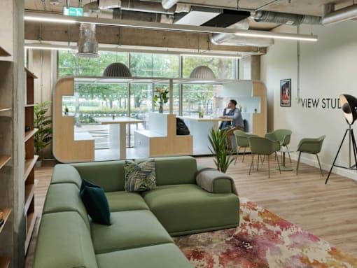 A room with a green couch and a person sitting on a chair.