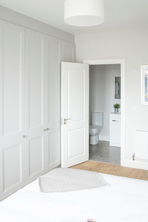 a white bedroom with white wardrobes and a bathroom with a toilet