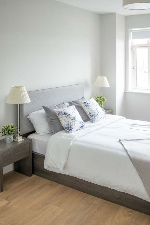 a bed with white sheets and pillows in a white bedroom