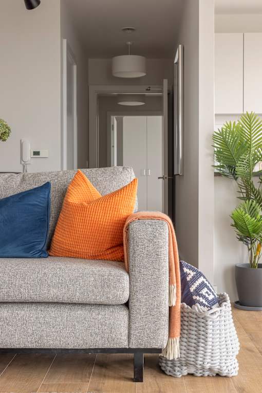 a living room with a grey couch with orange and blue pillows