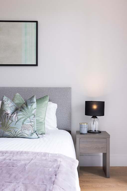 a bedroom with a bed with green pillows and a nightstand with a lamp