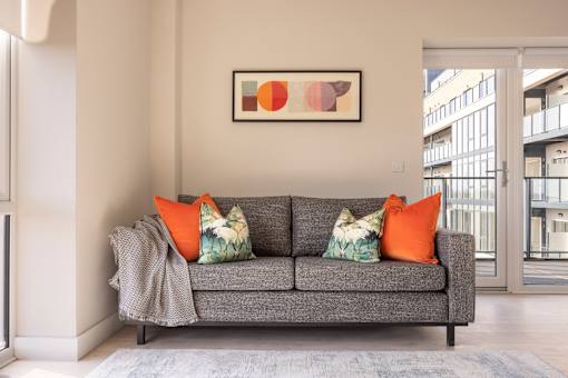 a living room with a grey couch and orange pillows