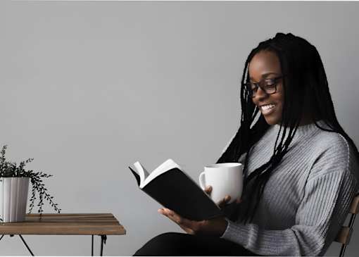 a woman reading a book while holding a cup of coffee