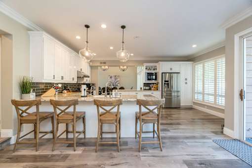 A kitchen with a white counter top and wooden chairs.