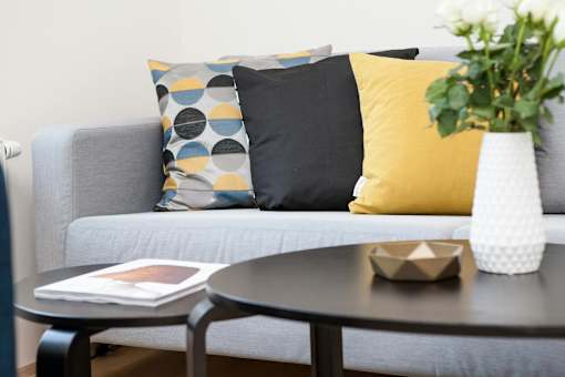 A grey couch with a yellow pillow and a vase with white flowers on a table.