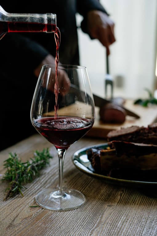 a person pouring red wine into a wine glass on a table