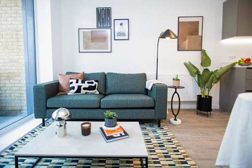 A living room with a green couch, a white coffee table, and a white lamp.