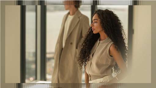 A woman with curly hair stands in front of a window.