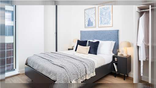 A bed with a blue headboard and a grey and white blanket is in the image.