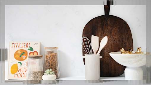 A kitchen counter with a cutting board, a book titled Italian Style Food, and some jars of spices.