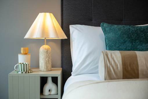 A white bed with a green pillow and a lamp on a nightstand.