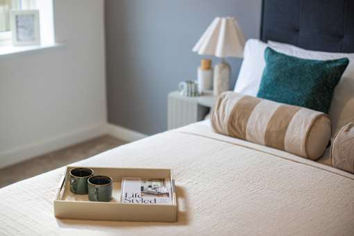 A tray with two cups and a magazine on a bed.