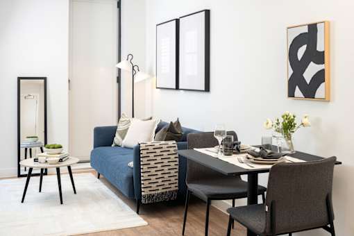 A modern living room with a blue couch, a black chair, and a dining table set for two.