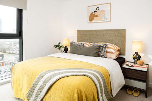 A bedroom with a bed covered in a yellow comforter and pillows.