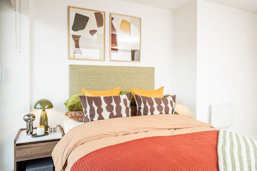 A bed with a red comforter and a green headboard with two framed pictures above it.