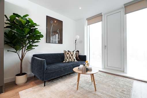 A living room with a blue couch, a potted plant, a coffee table, and a painting on the wall.