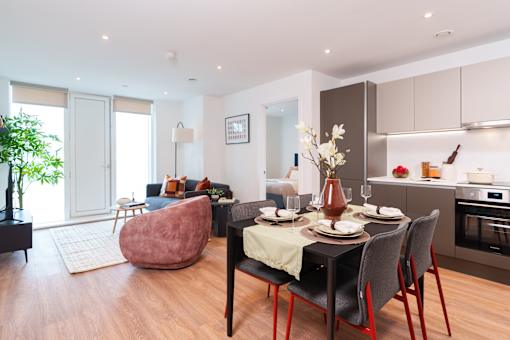 A modern dining room with a table set for two and a kitchen area in the background.