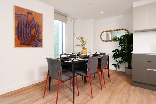 A dining room with a table set for four and a painting on the wall.