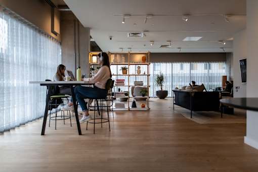 Two women sitting at a table in a brightly lit room with wooden floors and white walls.at Slate Yard Apartments, Salford
