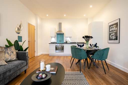 a living room with a table and a couch and a kitchen at The Keel Apartments, Liverpool